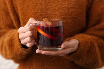 Woman holding glass cup of hot mulled wine at home, closeup