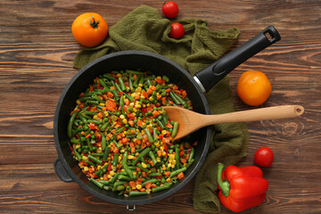 Frying pan with roasted vegetables on wooden background