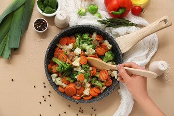 Young woman and tasty roasted vegetables in frying pan on beige background