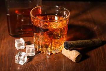 Glass of rum with ice cubes and cigar on wooden background
