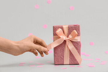 Female hand with gift box and pink confetti on grey background
