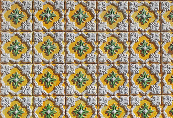 Close-up of traditional Portuguese ceramic tiles with embossed yellow, green and white patterns. Classic azulejos texture with ornamental relief. For backgrounds, prints, packaging, or design.