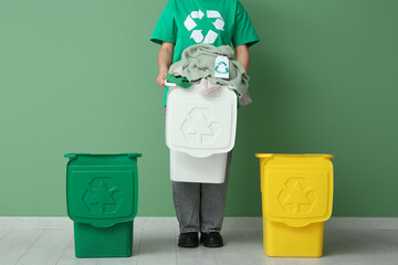 Female activist holding recycling bin with clothes on green background