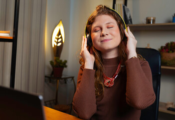 Redhead woman enjoying music with headphones while working from home. A relaxed and cheerful moment...