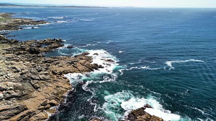 Experience an absolutely stunning aerial view of rocky shores seamlessly blending with vibrant blue...