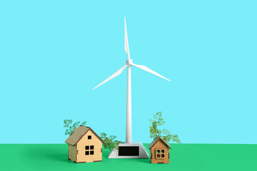 Wind turbine with house models on table against blue background. Green technology concept
