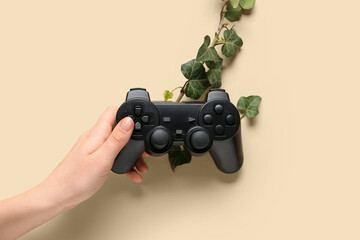 Female hand with game pad and plant leaves on beige background. Green technology concept © Pixel-Shot
