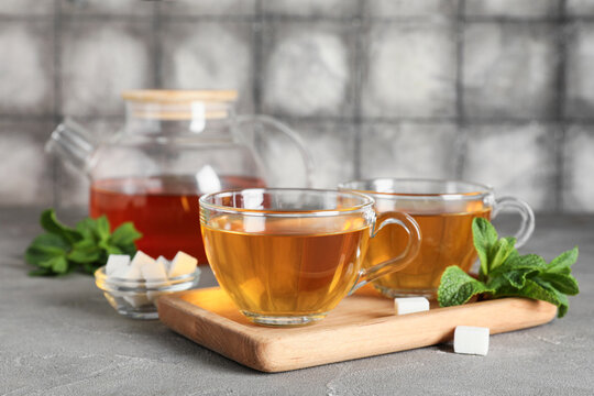 Glass cups of hot mint tea and bowl with cubes of sugar on grey table