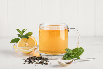 Glass cup of hot mint tea with lemon and dry leaves on white table