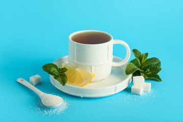 Cup of hot mint tea with sugar and lemon slice on blue background