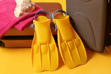 Flippers, suitcases, towel and seashell on color background