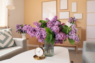 Vase with lilac flowers and alarm clock on table in living room