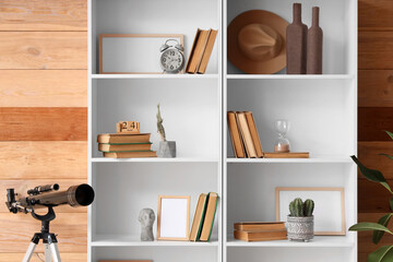 Bookshelf with decor, telescope and cacti near wooden wall in room