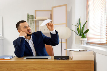 Bored businessman with paper plane at table in office