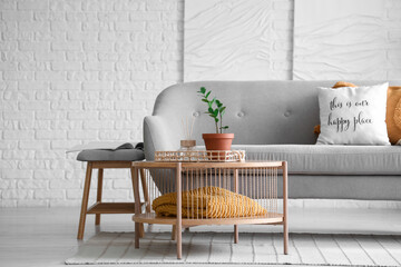 Grey sofa and wooden coffee table near white brick wall in interior of living room