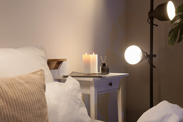 Burning candles with magazine and reed diffuser on table in dark bedroom
