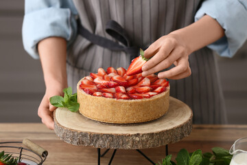 Woman decorating sweet strawberry tart in kitchen