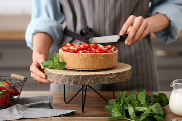 Woman cutting sweet strawberry tart in kitchen