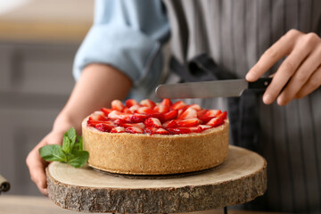 Woman cutting sweet strawberry tart in kitchen