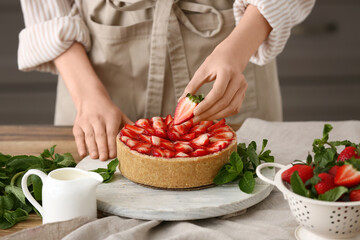 Woman decorating sweet strawberry tart in kitchen, closeup