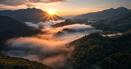 Aerial video shows a mountain range shrouded in early morning mist bathed in golden sunrise light - Powered by Adobe