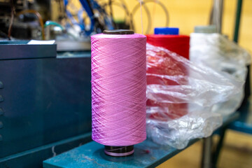 Pink yarn spool with red and white threads in a textile factory. the vibrant colors and industrial setting highlight manufacturing and craftsmanship trends.