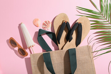 Composition with stylish wicker flip-flops, bag, bottle of sunscreen cream and green leaf on pink...