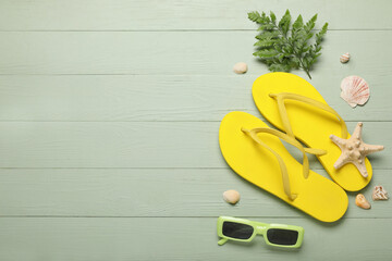 Composition with stylish flip-flops, sunglasses, paddles and seashells on green wooden background