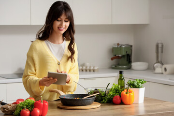 Young woman with recipe book on tablet computer cooking in kitchen