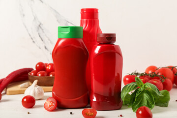 Bottles of tasty ketchup with basil leaves and garlic on white wooden table