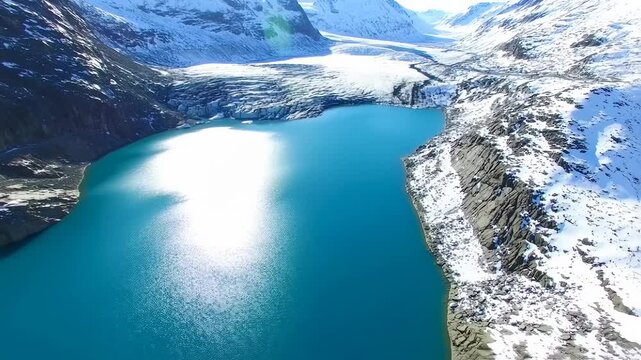 Aerial footage captures turquoise lake and glacier against snow mountain