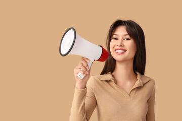 Smiling young woman with megaphone on beige background