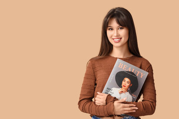 Smiling young woman with fashion magazine on beige background