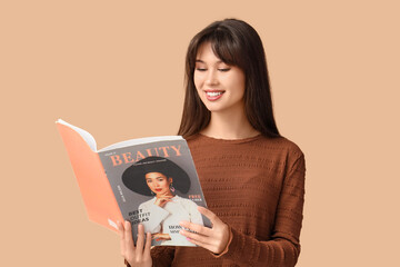 Smiling young woman reading fashion magazine on beige background