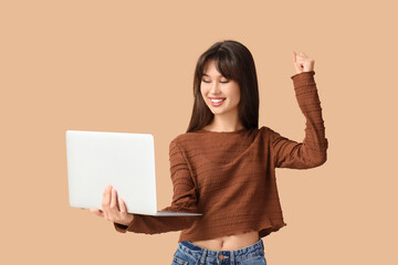 Smiling young woman with laptop on beige background