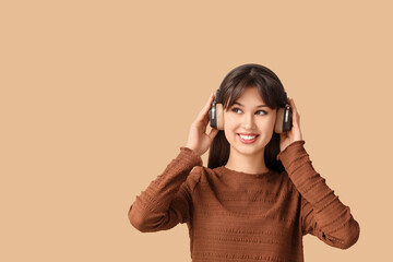 Smiling young woman in headphones listening to music on beige background
