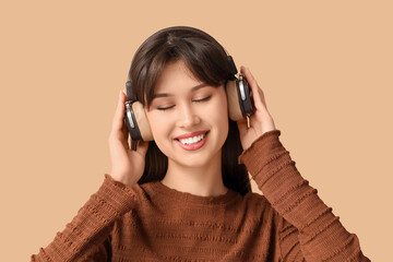 Smiling young woman in headphones listening to music on beige background, closeup