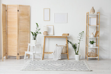 Interior of light room with blank frames, table and folding screen