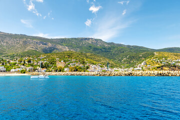 Fototapeta premium Agios Kirykos harbor port waterfront cityscape and sailboat by Icarian sea and church on Ikaria, Greece Greek longevity blue zone island from ferry