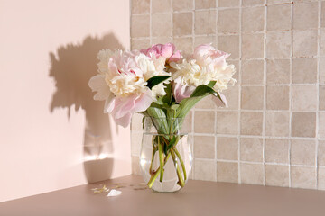 Vase with beautiful peony flowers on table near pink tile wall