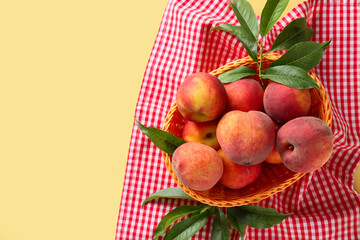 Wicker basket of fresh peaches on yellow background