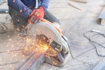 A worker is cutting a steel beam with a cut-off saw, producing sparks.