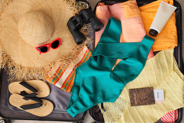 Open suitcase with beach accessories on carpet, top view