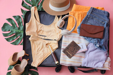 Open suitcase with beach accessories and palm leaves on pink background, top view