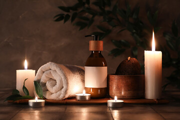 Composition with burning candles, bottle of cosmetic product and spa stones on grey tile...