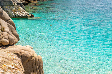 Seychelles beach at Magganitis, Ikaria island Greece, Icarian sea with crystal clear green turquoise water man people swimming by rocky cliffs coast