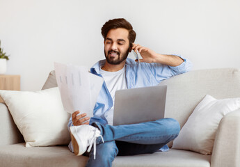 Eastern Freelancer Man With Cellphone, Papers And Laptop Working Remotely At Home. Millennial Arab...