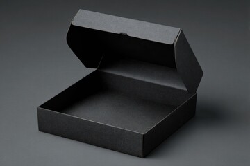A partially opened square black cardboard box sits on a dark gray surface, showcasing its empty interior and textured exterior.  The lighting is subtly dramatic