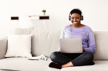 Rest And Relax Concept. Smiling curvy african american woman sitting on the couch and using laptop,...