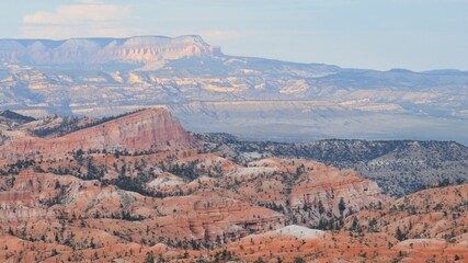 Expansive view of Bryce Canyon&rsquo;s colorful ridges and pine-dotted cliffs, with layered mesas and mountains in soft evening light.